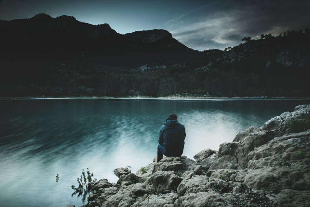 Comment reconnaître une dépression ? dépression a man sits on a rock staring across a lake at dusk