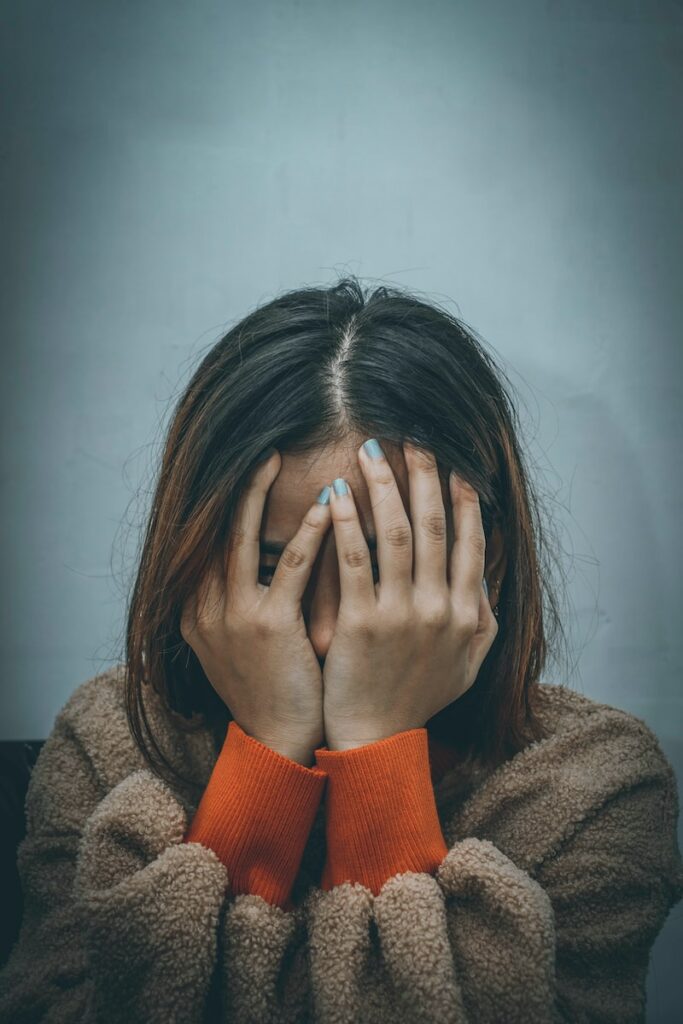 maladie chronique woman in brown sweater covering her face with her hand