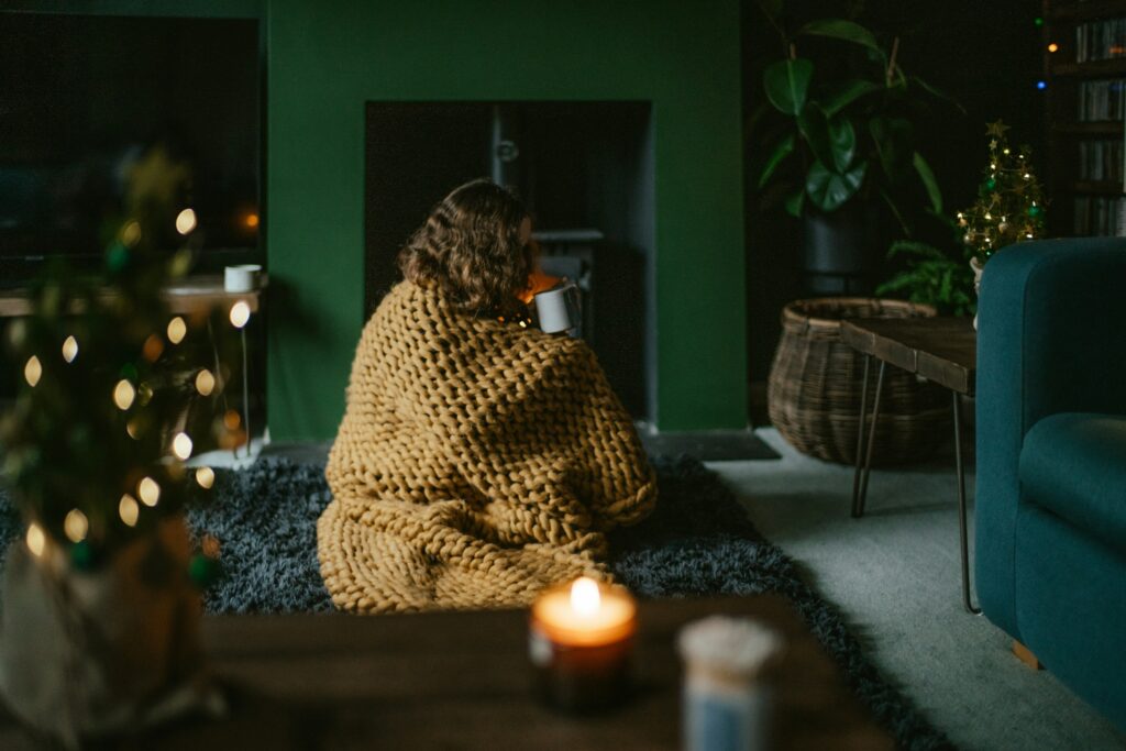 Coup de blues : comment l’identifier et s’en libérer naturellement Femme assise sur un tapis dans son salon. Elle boit son thé en se réchauffer près de la cheminée