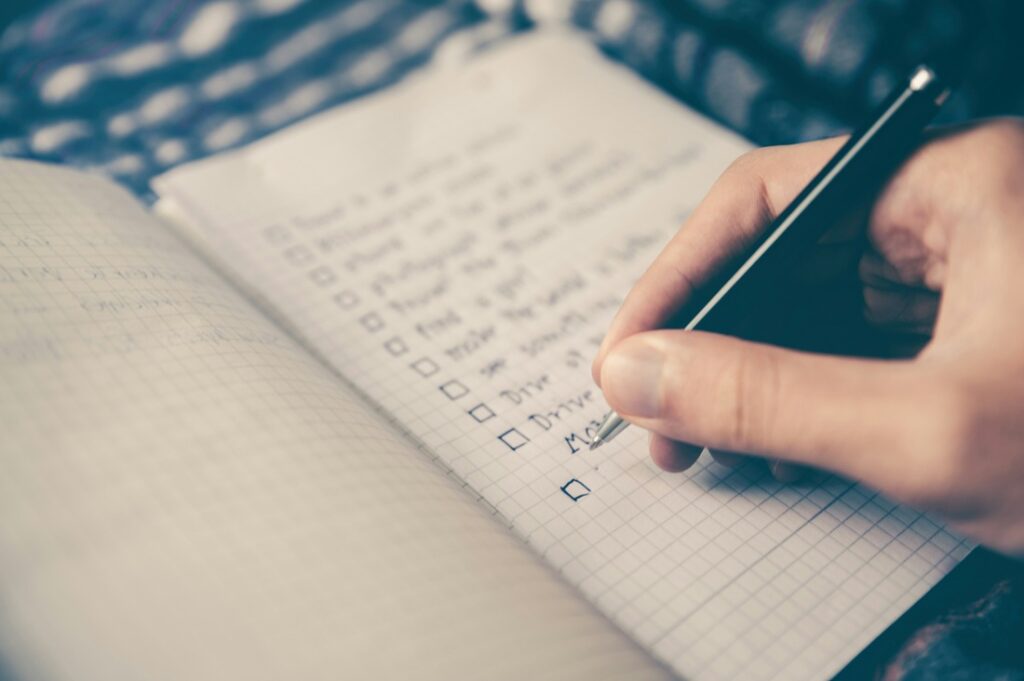 Comment Être Sûr de Soi : 15 conseils actionnables dès aujourd’hui Une main qui rempli une liste à réaliser sur un carnet